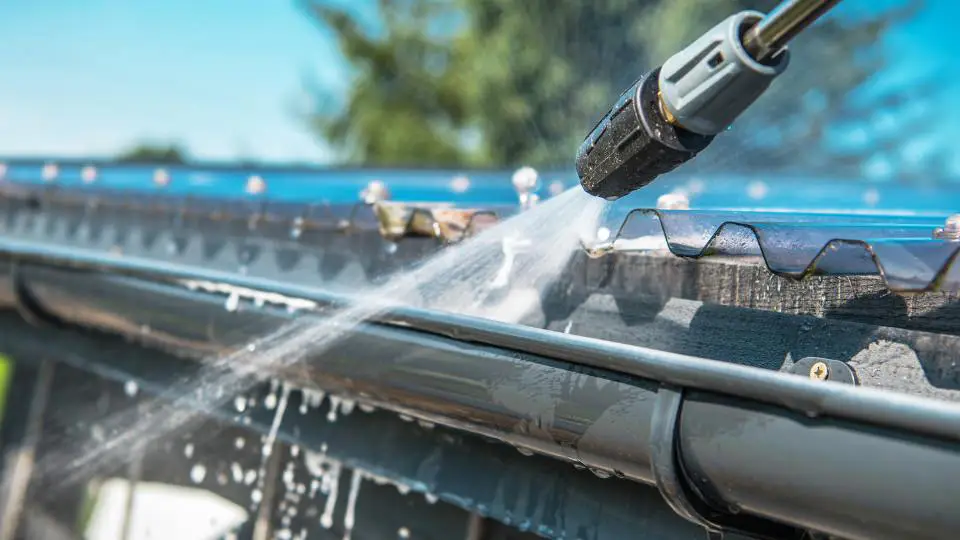 Close-up of a power washing tool cleaning a seamless gutter installed on a residential home, demonstrating effective maintenance.